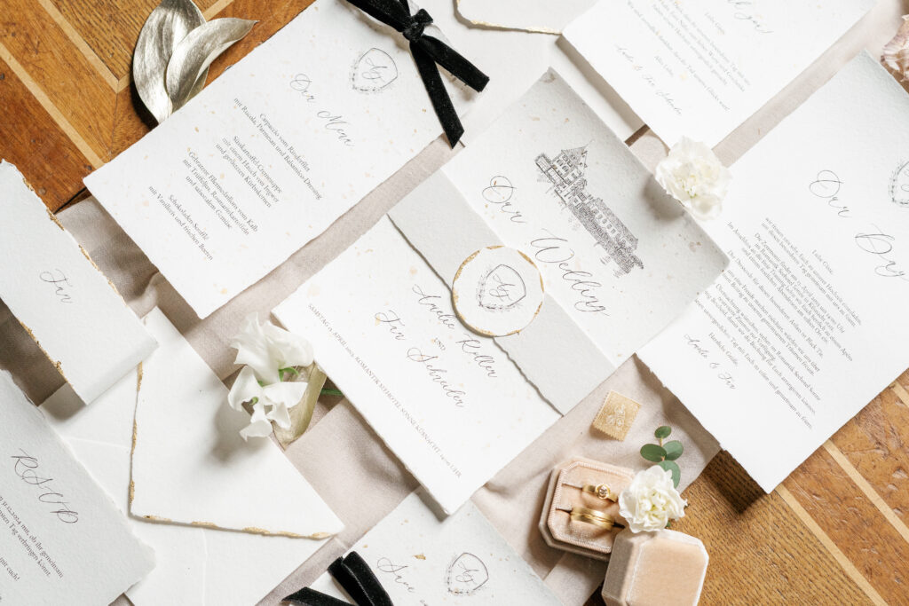 Flatlay von luxuriöser Hochzeitspapeterie auf handgeschöpftem Papier mit Blattgold und handgemalter Illustration