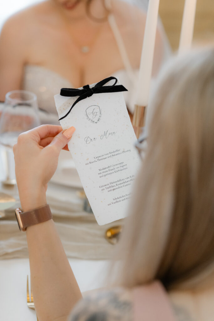 Hochzeitsgast hält elegante Menükarte in der Hand mit personalisiertem Wappen