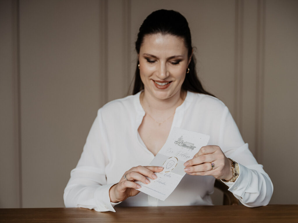 Designerin für Hochzeitspapterie hält Hochzeitseinladung in der Hand mit personalisiertem Hochzeitslogo